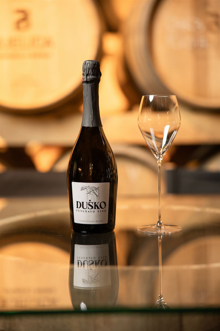 Boca penušavog vina Duško sa čašom ispred barik buradi